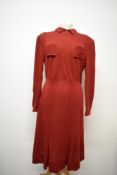 A russet coloured 1940s day dress, having long sleeves, pockets to bodice with angular stitched