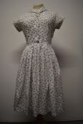 A 1950s cotton day dress, having pleated skirt, side metal zip and buttons to front, Swiss label