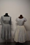 Two 1950s dresses, comprising grey checked cotton day dress and white lace dress with blue lining.