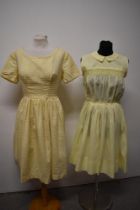 Two 1950s yellow day dresses, one of sheer floaty fabric, having embroidery to bodice and pleats