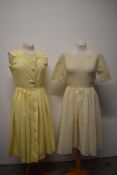 Two pale yellow 1950s day dresses, one of textured cotton and the other a synthetic semi sheer