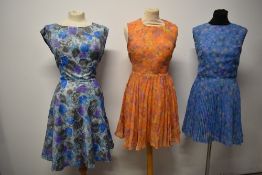 Three floaty abstract patterned day dresses, two having concertina pleats, one with belt.