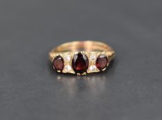 A garnet trio ring interspersed by white stones, possibly sapphires in a moulded gallery mount on