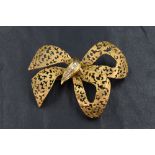 A large 18ct gold brooch in the form of a bow having a damask pattern with diamond chips to the