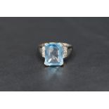 A facet cut rectangular blue topaz ring having a four claw raised mount and diamond chip set