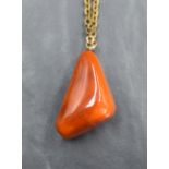 A large amber style pendant of triangular form on a yellow metal chain, 30.7g