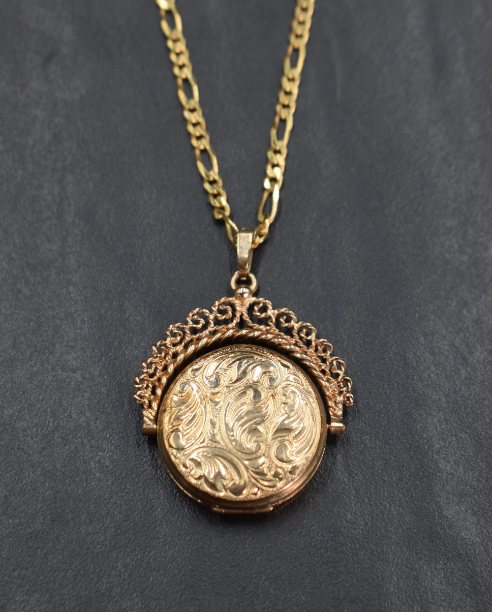 A 9ct gold spinning locket having floral motif engraving with a decorative rope-work frame, on a 9ct