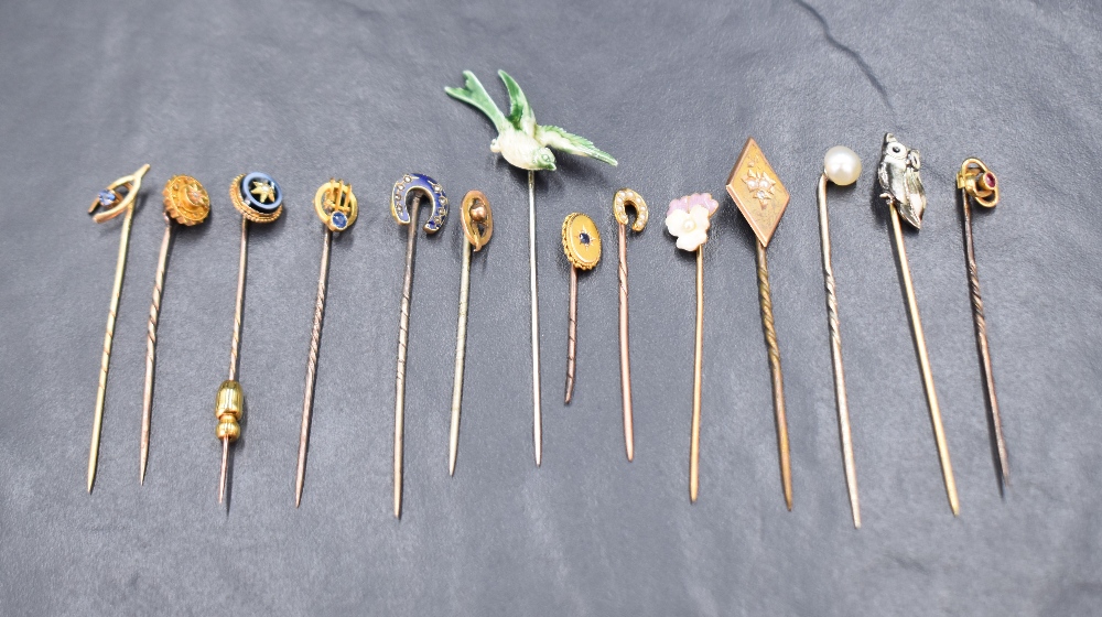 A collection of yellow metal stick pins including an enamel and diamond set horse shoe, a seed pearl