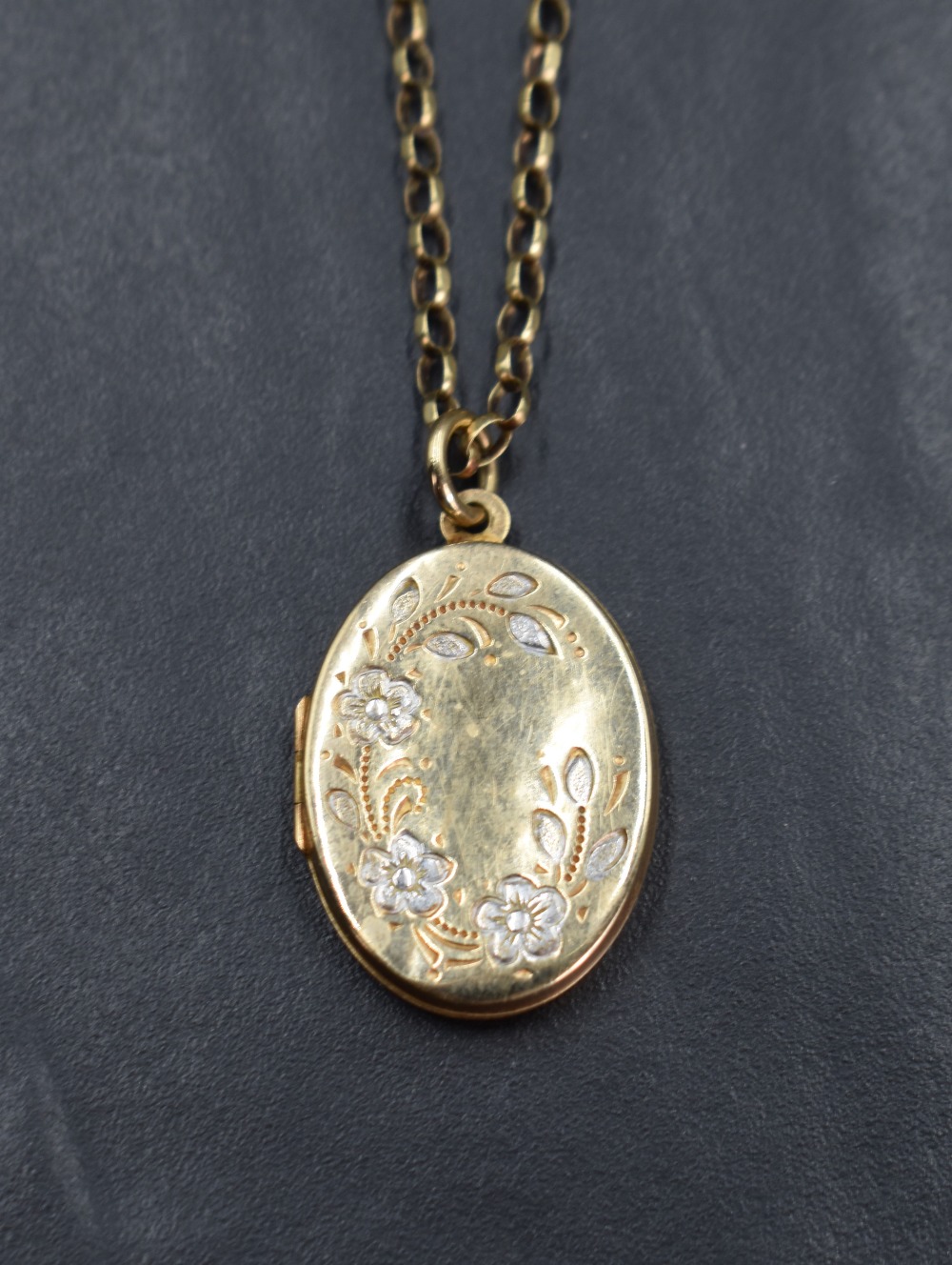 A yellow metal oval locket having a decorative floral design engraving on a 9ct gold rolo chain, 7.