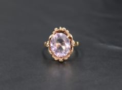 An oval amethyst ring having a four claw setting in decorative moulded surround on a yellow metal