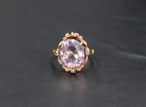 An oval amethyst ring having a four claw setting in decorative moulded surround on a yellow metal