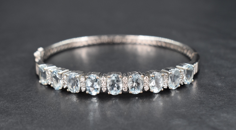 An 18ct white gold, aqua marine and diamond hinged bangle having nine brilliant cut aqua marines