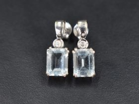 A pair of 18ct white gold stud earrings having small collared diamond drops to baguette cut Aqua