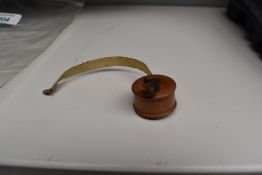 A miniature novelty wooden fly fishing reel holding a tape measure