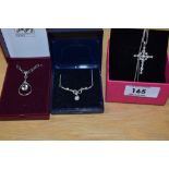 A collection of silver necklaces comprising a cubic zirconia set stylised cross, an open teardrop