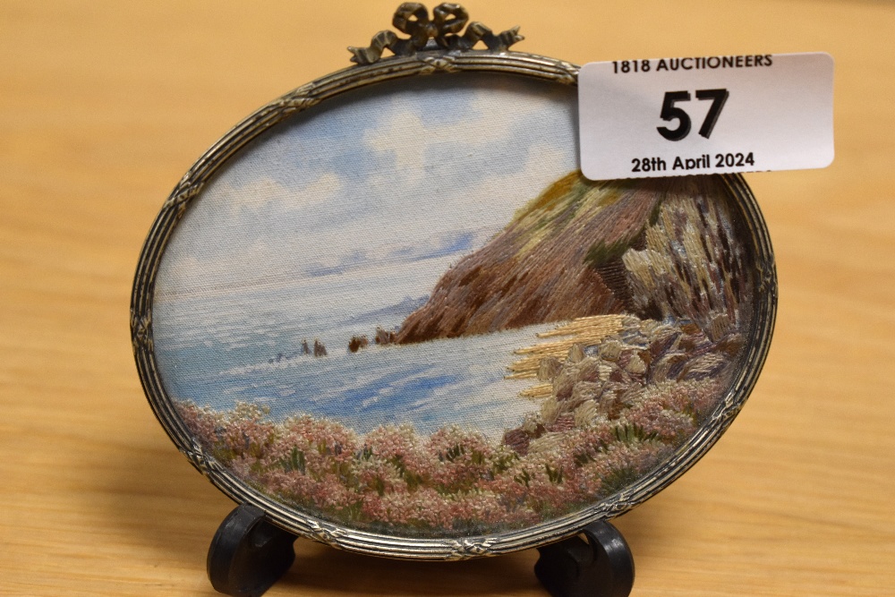 A 20th Century miniature needlework, oval shaped and depicting a coastal landscape, displayed within