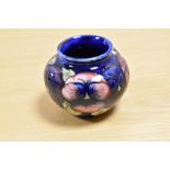 A William Moorcroft squat vase, in the Pansy pattern against a blue ground, measuring 6.5cm tall