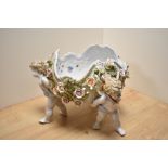 A Dresden porcelain figural centre-piece, formed as three three winged cherubs holding a flower