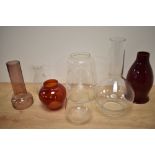 An assorted collection of clear and coloured glass oil lamp shades and chimneys, including a