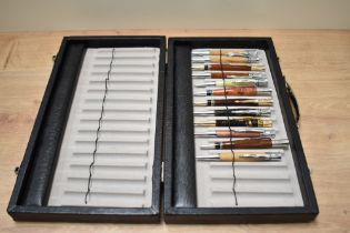 A storage case containing twelve hand made ballpoint pens in various turned woods and resins