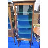 A late 19th or early 20th Century mahogany display cabinet of narrow proportions, having scroll
