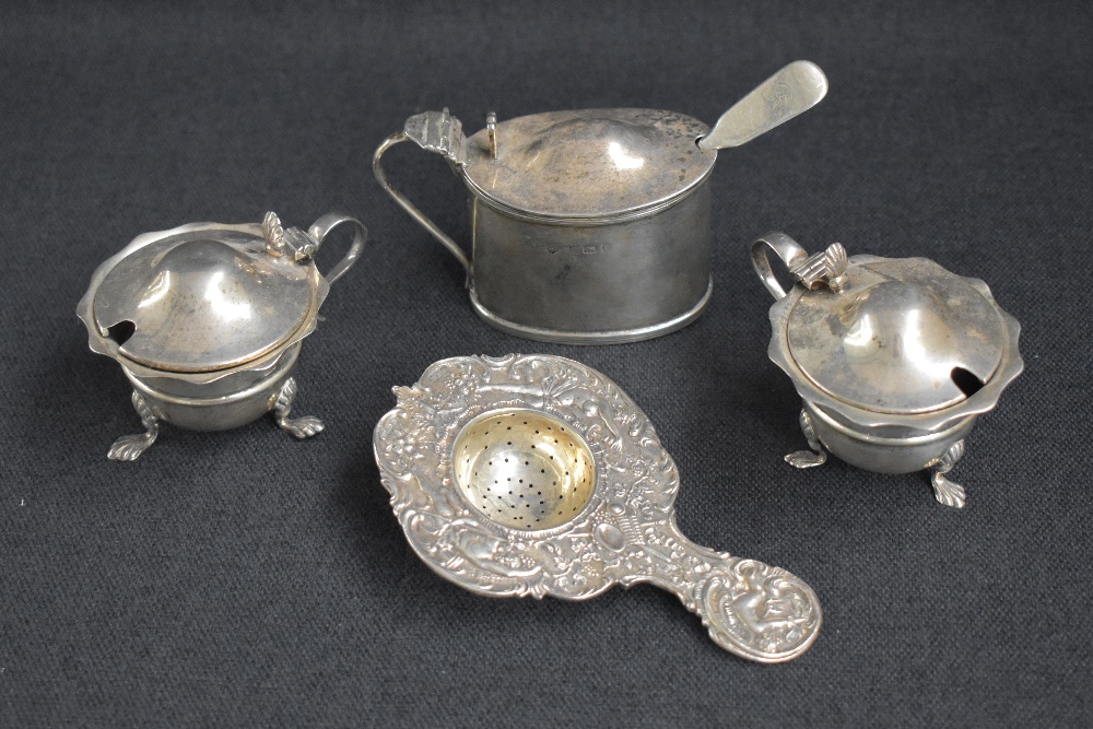 A group of silver table wares, comprising a decorative embossed tea strainer having cherubs and