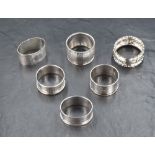 A group of six silver napkin rings, five having engine turned decoration and cartouches, the other