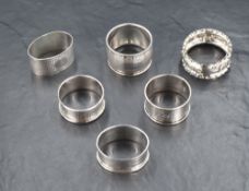 A group of six silver napkin rings, five having engine turned decoration and cartouches, the other