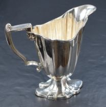 An Edwardian silver cream jug, of fluted helmet form with conforming foot scrolled angular handle,