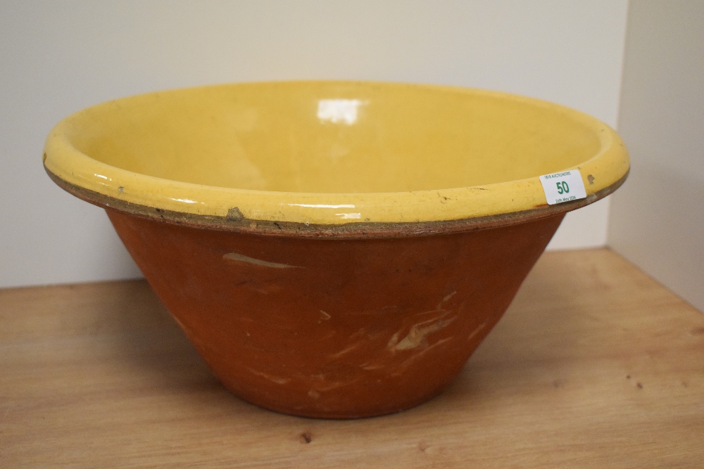 A large antique terracotta bowl with yellow glaze to inside.