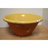 A large antique terracotta bowl with yellow glaze to inside.