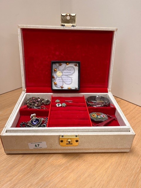 A cream jewellery box with red velvet lining, containing an assortment of costume jewellery