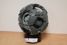 A Chinese carved green soap stone puzzle ball on treen stand, having foliate decoration.