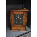 An Arts and Crafts oak smokers cabinet with embossed metal decoration to door, with internal