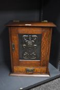 An Arts and Crafts oak smokers cabinet with embossed metal decoration to door, with internal