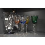 Two glass water jugs and four coloured wine glasses, in shades of green, purple, pink and yellow.