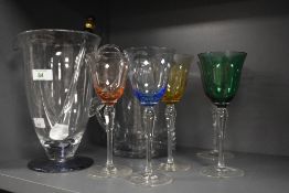 Two glass water jugs and four coloured wine glasses, in shades of green, purple, pink and yellow.