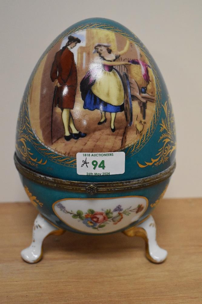 A Continental porcelain footed egg trinket box, decorated with vignettes of floral arrangements