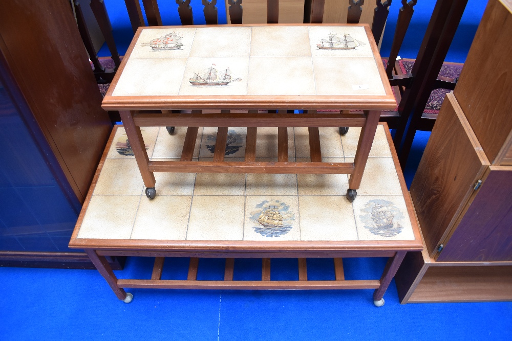 Two graduated teak and tile top coffee tables on castors with slatted undershelves