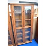 A modern pine glass fronted slim bookcase