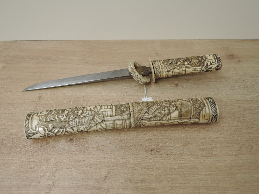 A Japanese Dagger with highly carved bone hilt and scabbard depicting Village People & Houses, blade