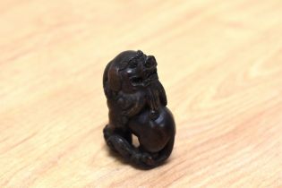 A Japanese carved hardwood Netsuke, depicting a Temple lion holding ball, with inset bone