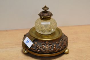 An antique embossed copper and brass based desk top ink well, with cut glass ink well.