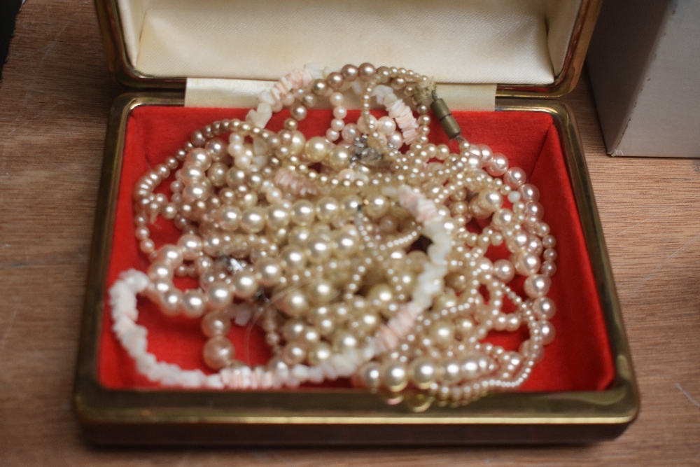 A red faux crocodile jewellery box containing an assortment of imitation pearl necklaces and a
