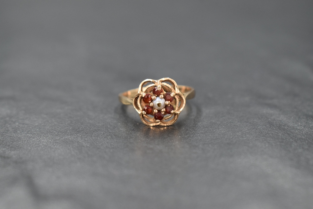 A 9ct gold garnet and seed pearl cluster ring in an open frilled mount, damage to pearl and loop
