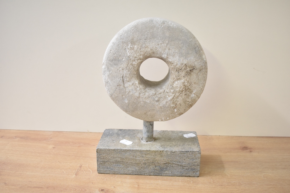 A heavy stone disc sculpture standing on a rectangle block base, h30cm