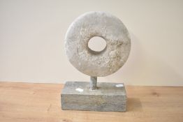 A heavy stone disc sculpture standing on a rectangle block base, h30cm