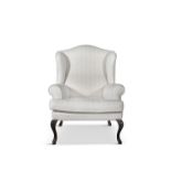 A WINGBACK ARMCHAIR, upholstered in cream fabric, raised on short mahogany cabriole legs.