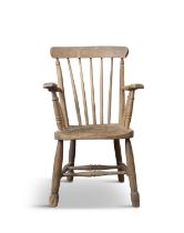 A PINE CURVED RAILBACK ARMCHAIR the stick back, flat armrests and dished saddle seat on splayed