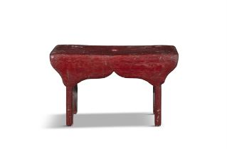 A RED PAINTED PINE LOW RECTANGULAR STOOL with shaped apron on panel end supports. 25cm high,